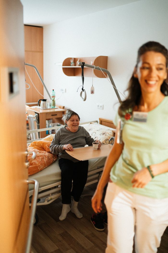 Services Smiling nurse assists senior patient in a cozy hospital room, promoting healthcare and wellbeing.
