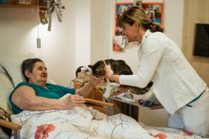 A caregiver shares a gentle moment with a cat and a senior resident, fostering connection and happiness in a retirement home.