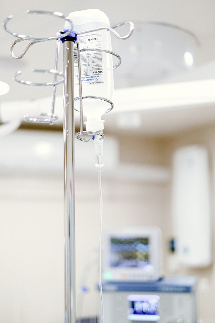 About Close-up of an IV drip in a sterile hospital setting with background medical equipment.