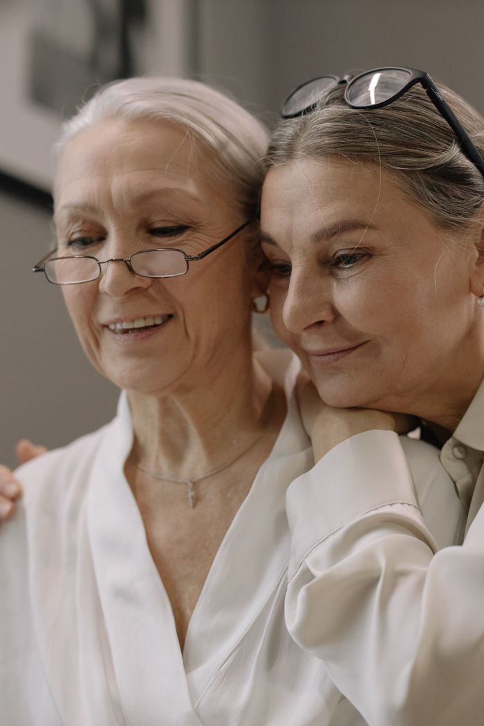 Mastering the First Impression: Your intriguing post title goes here Two senior women embracing and smiling indoors, showcasing friendship and joy.